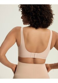 Bezzespolowy biustonosz w jasnym beżu, z szerokimi ramiączkami, gładką teksturą i zapięciem na haftki z tyłu. Bezszwowa konstrukcja i miękki materiał.