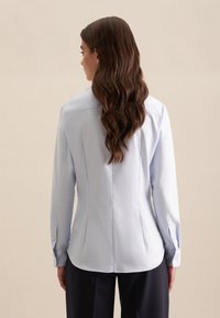 Lichtblauwe blouse met lange mouwen in een getailleerde pasvorm, voorzien van een achterste inzetstuk en knoopmanchetten, gemaakt van gladde stof.