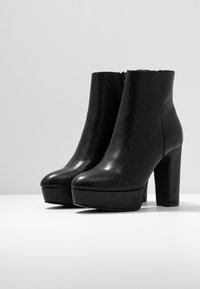 Black leather ankle boots with a smooth finish, square toe, high block heel, and platform sole. Zipper closure on the back.