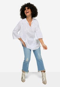 Hvid broderet bluse med brede ærmer, parret med lyse denimjeans med frynser i kanten og farverige perleaccenter, samt metalliske ankelstøvler.
