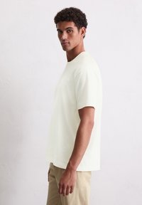 Helles, gelbes, kurzärmeliges T-Shirt aus weichem Stoff mit Rundhalsausschnitt und lockerer Passform, kombiniert mit beigen Hosen.