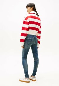 Czerwono-biała, paskowana, krótka bluza w połączeniu z dopasowanymi niebieskimi dżinsami i białymi sneakersami z srebrnymi akcentami. Widok z tyłu, gładka faktura.