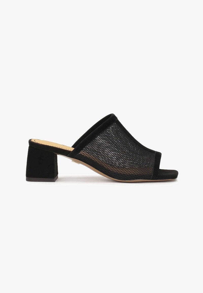 Mules à bout ouvert en mesh noir avec un talon bloc. Une douce bordure en suède noir souligne la partie supérieure et les bords, ajoutant texture et contraste.