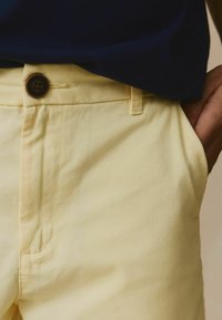 Ljust gula tygshorts med en slät yta, med en knappmidja, sidofickor och subtila sömdetaljer.