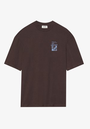 T-shirt en coton marron avec un graphique floral bleu sur le côté gauche de la poitrine. Manches courtes et coupe décontractée, avec un col rond.