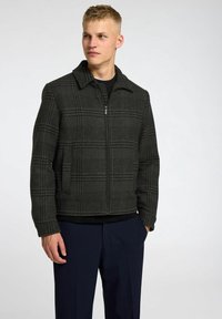 Veste à carreaux gris avec fermeture éclair sur le devant, col structuré, poches latérales et poignets côtelés. Matériau lisse avec un fini texturé.
