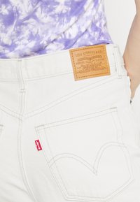 Jeans de mezclilla blanca con una etiqueta de cuero de Levi Strauss & Co., con costuras en contraste y bolsillos traseros con diseño curvado característico.