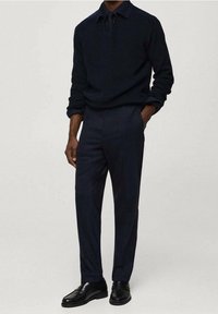 Maglione blu scuro con scollo a V, abbinato a pantaloni su misura dello stesso colore e scarpe in pelle nere, caratterizzati da una texture liscia e linee pulite.