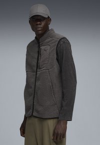 Fleece-Weste in Dunkelgrau mit Reißverschluss auf der Vorderseite, ausgestattet mit einer gestickten Tasche und glatten schwarzen Akzenten, kombiniert mit einer grauen Mütze.