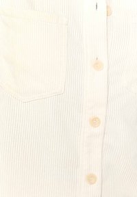 Cream-colored ribbed shirt with a flap pocket, button-front closure, and clear plastic buttons. Visible vertical texture throughout the fabric.