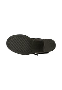 Černá podrážka boty s texturovaným vzorem protiskluzu a malým podpatkem, pohled zespodu na bílém pozadí.