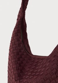 Burgundia kootud käekott, millel on tekstuurne pind, kaarjas kuju ja üks rihm, millel on tõmblukuga sulgemine ülemisel serval.