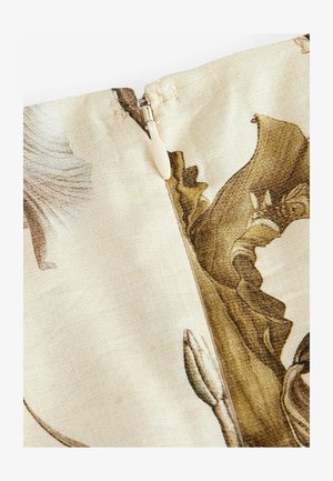 Tkanina s cvetnim vzorcem na bež ozadju, ki vključuje zadrgo in teksturne podrobnosti v rjavih in zlatih odtenkih.