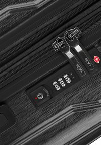 Schwarzer Hartschalenkoffer mit zwei silbernen Reißverschlüssen, einem Zahlenverschluss und strukturierter Oberfläche, ausgestattet mit einer roten Kontrollleuchte für zusätzliche Sicherheit.
