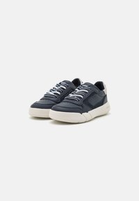 Sneaker in pelle blu con lacci bianchi, dettagli perforati e suola beige. Forma arrotondata con un leggero tacco e accenti testurizzati.