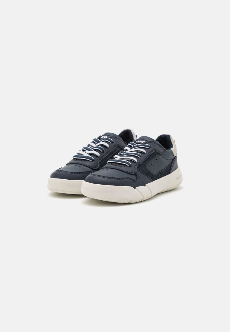 Zapatillas de cuero navy con cordones blancos, detalles perforados y suela beige. Forma redondeada con un ligero tacón y acentos texturizados.