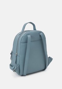 Light blue faux leather backpack with dual zippers, top handle, adjustable straps, and front pocket with tassel accents. Compact design.