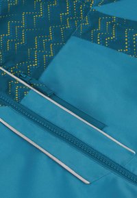 Türkisfarbener Stoff mit einem geometrischen Muster aus gelben Punkten und Linien. Beinhaltet einen sichtbaren Reißverschluss mit einem kontrastierenden Ziehband. Glatte Textur.