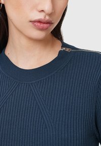 Laivastonsininen ribattu neulepaita, jossa on pyöreä pääntie ja pieni hopeinen vetoketju yksityiskohtana olkapäällä. Pehmeä rakenne ja istuva malli.