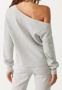 Light gray oversized sweatshirt featuring a one-shoulder design, soft texture, ribbed cuffs, and a relaxed fit, paired with matching pants.