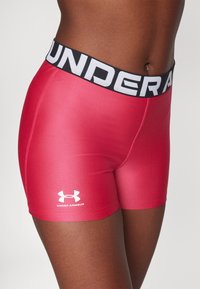 Rote Sporthosen aus glattem Material mit einem schwarzen Bund, der "UNDER ARMOUR" in weißer Schrift zeigt. Die Shorts haben ein glattes, enganliegendes Design.