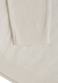 Manche de pull en maille couleur crème reposant sur un tissu de pull assorti avec des poignets et un ourlet côtelés.
