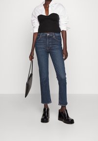 Top corto de canalé negro combinado con jeans de tiro alto azul, complementado con botas de tobillo de plataforma negra y un bolso negro elegante.