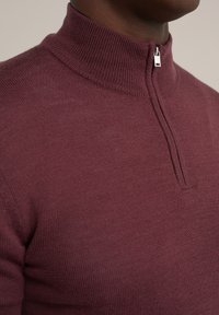 Burgundski pulover s pola patentom, sa rebrastim okovratnikom i finim pletenjem. Sadrži srebrni patentni zatvarač i prilagođen dizajn.