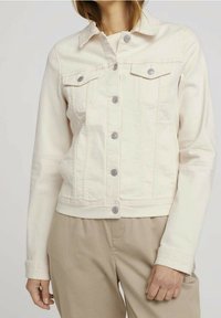 Giacca in denim beige chiaro con colletto, chiusura frontale con bottoni, due tasche sul petto e maniche lunghe. Presenta dettagli in metallo argentato.