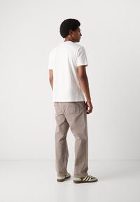 Hvit bomulls T-skjorte, avslappet passform, kombinert med lysebeige løstsittende bukser og grønt-randede sneakers. Enkelt design med minimale detaljer.