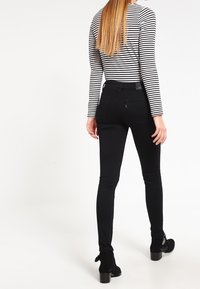 Jeans negros ajustados con una cintura de media altura y bolsillos traseros, combinados con una camisa de manga larga a rayas en blanco y negro. Botines negros.