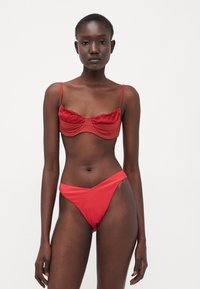 Set bikini rosso con top a balconcino arricciato e spalline sottili, completato da slip a vita alta. Tessuto liscio con un colore vivace.