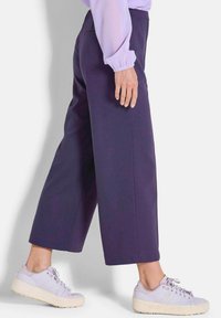 Marineblaue weite Hosen mit einer glatten Textur, hohe Taille und Seitentaschen, kombiniert mit hellvioletten Plateausneakern.