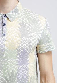 Polo à manches courtes avec un motif d'ananas pastel, doté d'un col à revers et de boutons bleus, confectionné en tissu doux et léger.