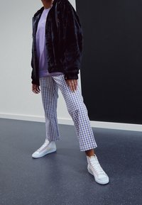 Sort faux fur jakke med lynlås, lavendel sweatshirt, lilla og hvidt ternet cropped bukser, hvide højhælede sneakers med pastelfarver.