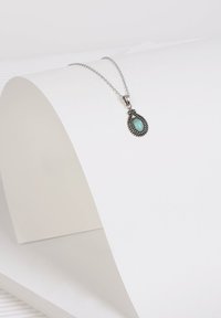 Zilveren ketting met een druppelvormige turquoise hanger, versierd met ingewikkelde kralen op de setting, hangend aan een fijne ketting.