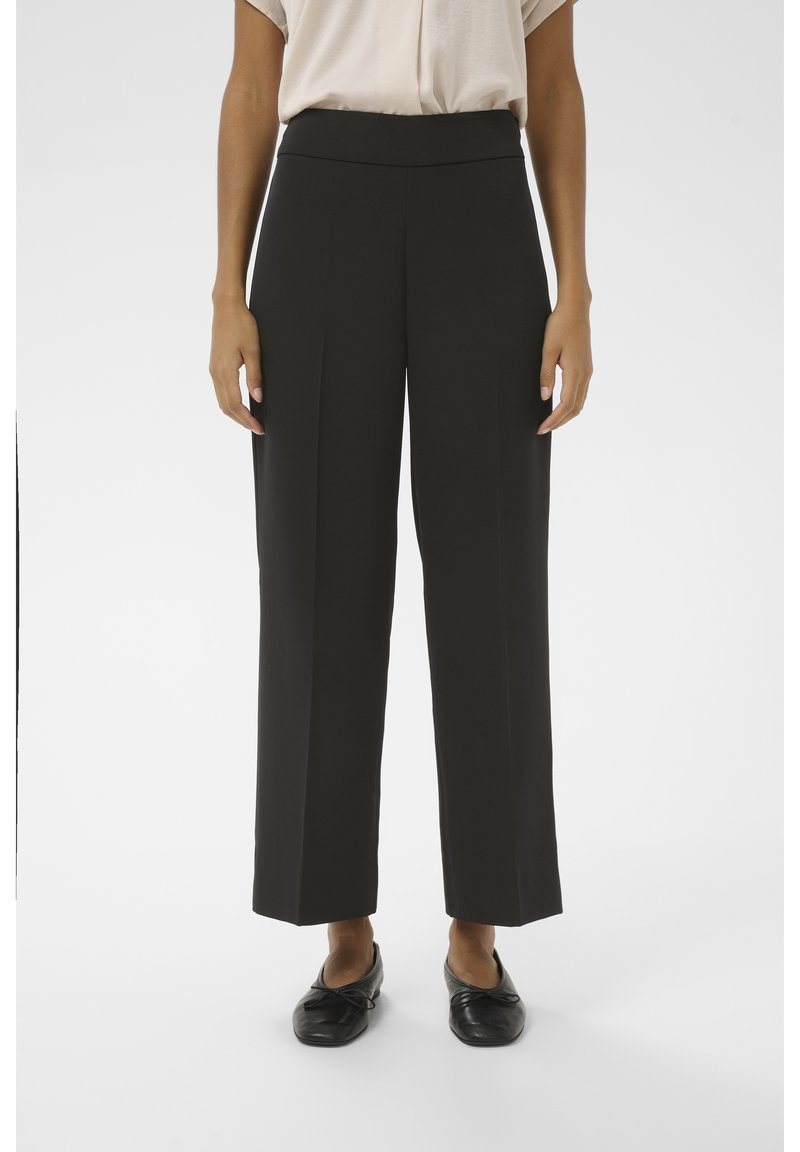 Svarta vida byxor med hög midja, med främre veck och en slät textur, kombinerade med svarta ballerinaskor.