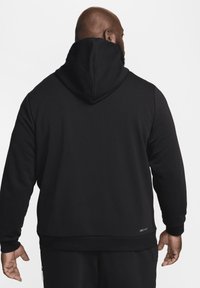 Felpa nera con cappuccio regolabile, texture uniforme, polsini e orlo a coste. Presenta un piccolo logo "DRI-FIT" in basso a destra.