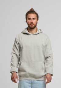 Sudadera con capucha gris claro hecha de una tela suave, que presenta un bolsillo tipo canguro y puños acanalados. Diseño simple y relajado sin patrones.