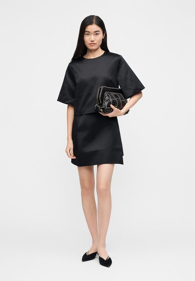 Melna satīna blūze ar īsām piedurknēm, kopā ar atbilstošu svārku. Modelis tur melanžas melnu maksīti ar ķēžu detaļām. Melnas plakanas kurpes.