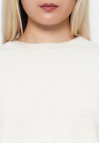 Biały sweter z dzianiny z okrągłym dekoltem, miękką teksturą i delikatnym pionowym szwem na plecach.