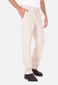 Pantaloni chiari in beige con una silhouette dritta, dotati di una parte anteriore piatta, due tasche laterali e una zip. Indossati con scarpe in camoscio marrone scuro.