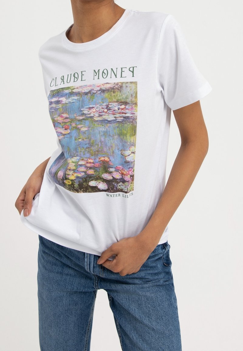 T-shirt en coton blanc avec une œuvre imprimée de "Nymphéas" de Monet, présentant des bleus, des verts et des roses vibrants, avec un texte vert en haut.