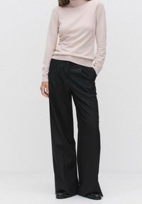 Maglione a collo alto rosa chiaro con maniche lunghe abbinato a pantaloni neri a vita alta e gamba larga. Tessuto liscio e senza motivi visibili.