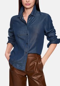 Dark denim shirt with a collared neckline, button-up front, and rolled sleeves, paired with brown leather pants. Smooth texture.