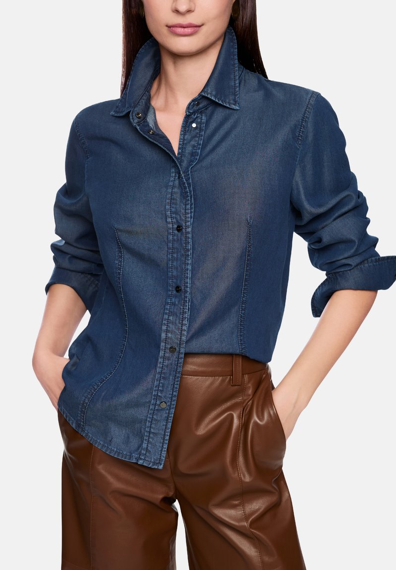 Dark denim shirt with a collared neckline, button-up front, and rolled sleeves, paired with brown leather pants. Smooth texture.