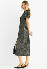 Black and gold patterned dress with short puff sleeves, side slit, and a fitted waist. Paired with black pointed-toe slingback shoes.