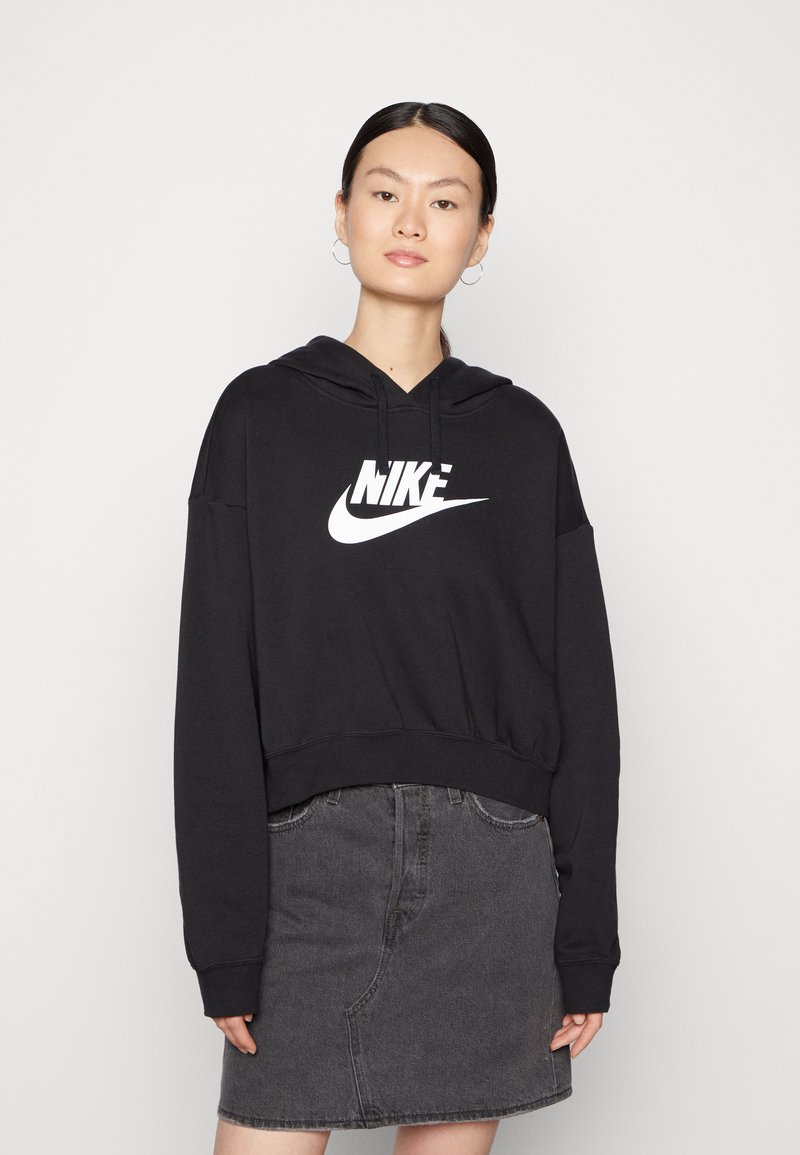 Sudadera negra recortada con un logo blanco de Nike, con capucha ajustable y mangas largas, combinada con una falda de mezclilla gris.