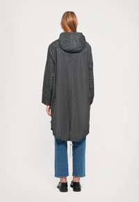 Zwart gemêleerd lang jack met capuchon, met een losse fit en trekkoorddetails aan de zoom, gecombineerd met lichtblauwe jeans en zwarte schoenen.