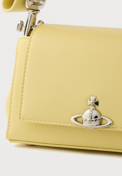 Κίτρινη τσάντα χειρός από δερματίνη με δομημένο σχεδιασμό, που διαθέτει μεταλλικό έμβλημα με θέμα πλανήτη και κομψές λεπτομέρειες ραφής.